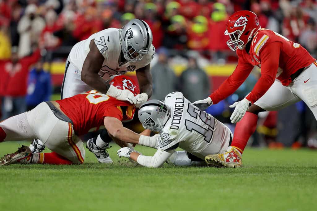 KANSAS CITY, MISSOURI - 29 NOVEMBER: Aidan O'Connell #12 dari Las Vegas Raiders kehilangan bola pada jepretan awal yang dipulihkan oleh Kansas City Chiefs di akhir kuarter keempat di GEHA Field di Stadion Arrowhead pada 29 November 2024 di Kansas City, Missouri.