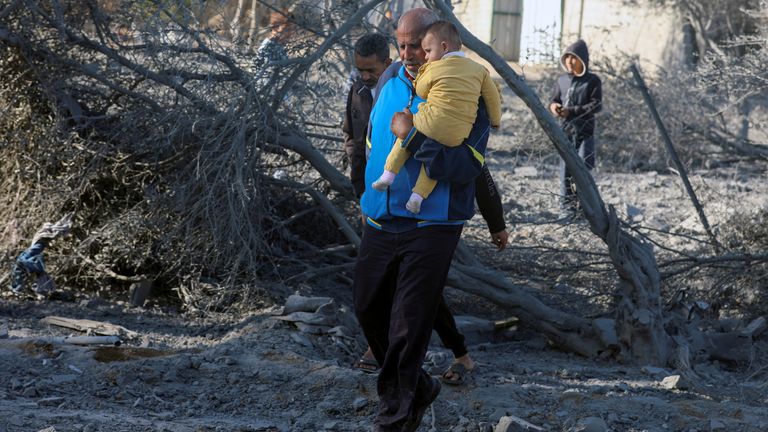 Seorang pria Palestina yang membawa seorang anak berjalan di lokasi serangan Israel di sebuah rumah di Deir Al-Balah di Jalur Gaza tengah. Foto Reuters