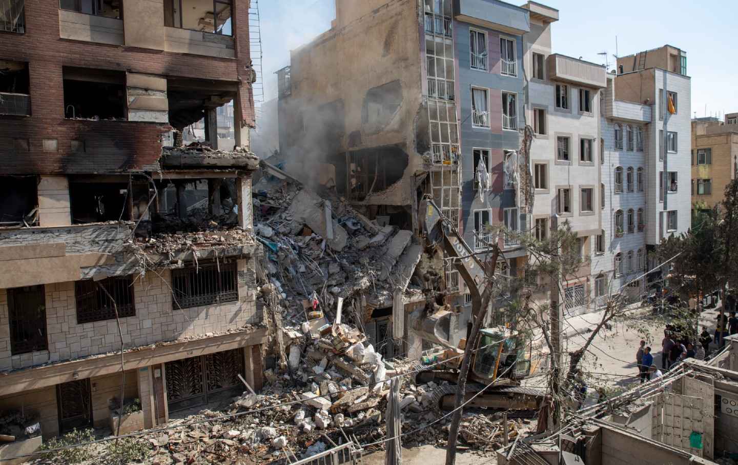 Sebuah ekskavator memindahkan puing-puing dari bangunan tempat tinggal yang hancur dalam serangan Israel di Teheran, pada 13 Juni 2025.