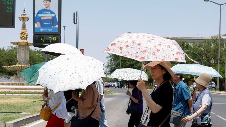 Orang-orang menggunakan payung di sebelah termometer yang menampilkan 47 derajat Celcius selama gelombang panas di Seville, Spanyol. Foto: Reuters