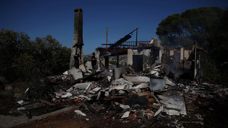 Seorang petugas pemadam kebakaran sukarela menggunakan selang untuk mendinginkan rumah yang terbakar selama kebakaran hutan di kota Koropi, dekat Athena. Foto: Reuters